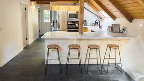 A modern kitchen with a central island, bar stools, and a sloped ceiling.