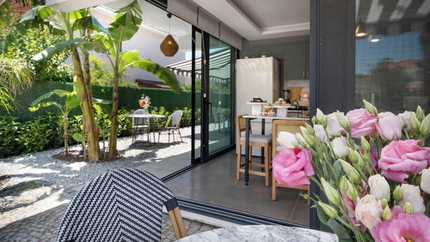 A modern kitchen with a dining area, large windows, and a garden with plants and a table. - Villa Lui Hotel Alaçatı (Cesme)