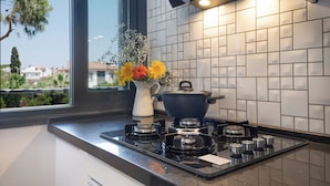 A modern kitchen with a gas stove, a white vase with flowers, and a window overlooking a residential area. - Villa Lui Hotel Alaçatı (Cesme)