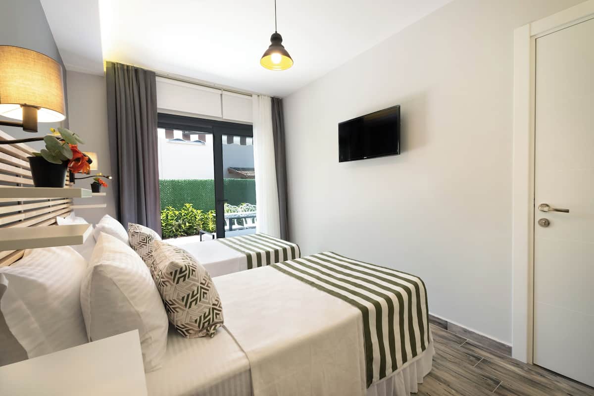 Ein Hotelzimmer mit Bett, Nachttisch, Lampe, Fernseher und einem Fenster mit Vorhängen.