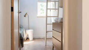 Un pasillo estrecho con techo inclinado, una escalera, una cama, un escritorio y un aparador.