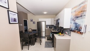A compact kitchen with a refrigerator, microwave, and sink. There is a dining table with chairs and a small rug.
