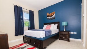 A bedroom with a bed, a nightstand, a lamp, a window with curtains, and a painting on the wall.