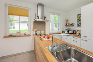 Een moderne keuken met een roestvrijstalen spoelbak, een houten aanrechtblad en een raam met uitzicht op een tuin.