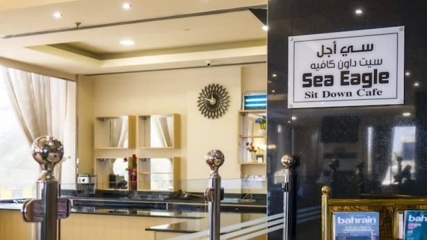 A cafe interior with a sign reading "Sea Eagle Sit Down Cafe" in Arabic and English. - oyo 123 (Manama)