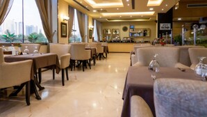 A restaurant with tables and chairs, a bar area, and a view of buildings. - oyo 123 (Manama)