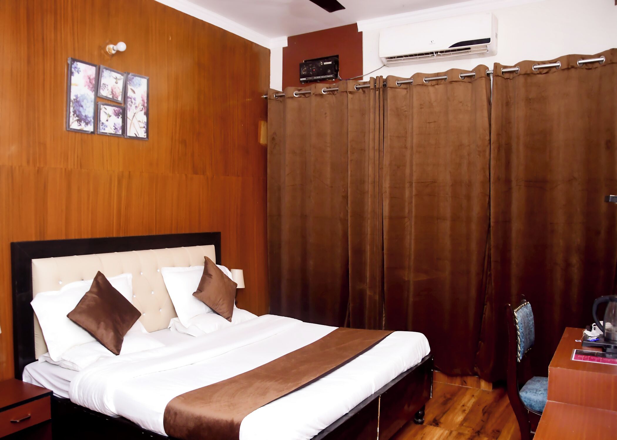 Ein Hotelzimmer mit einem Bett mit Holz-Kopfstück, einem braunen Vorhang und einem Schreibtisch mit Stuhl.