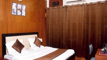 Ein Hotelzimmer mit einem Bett mit Holz-Kopfstück, einem braunen Vorhang und einem Schreibtisch mit Stuhl.