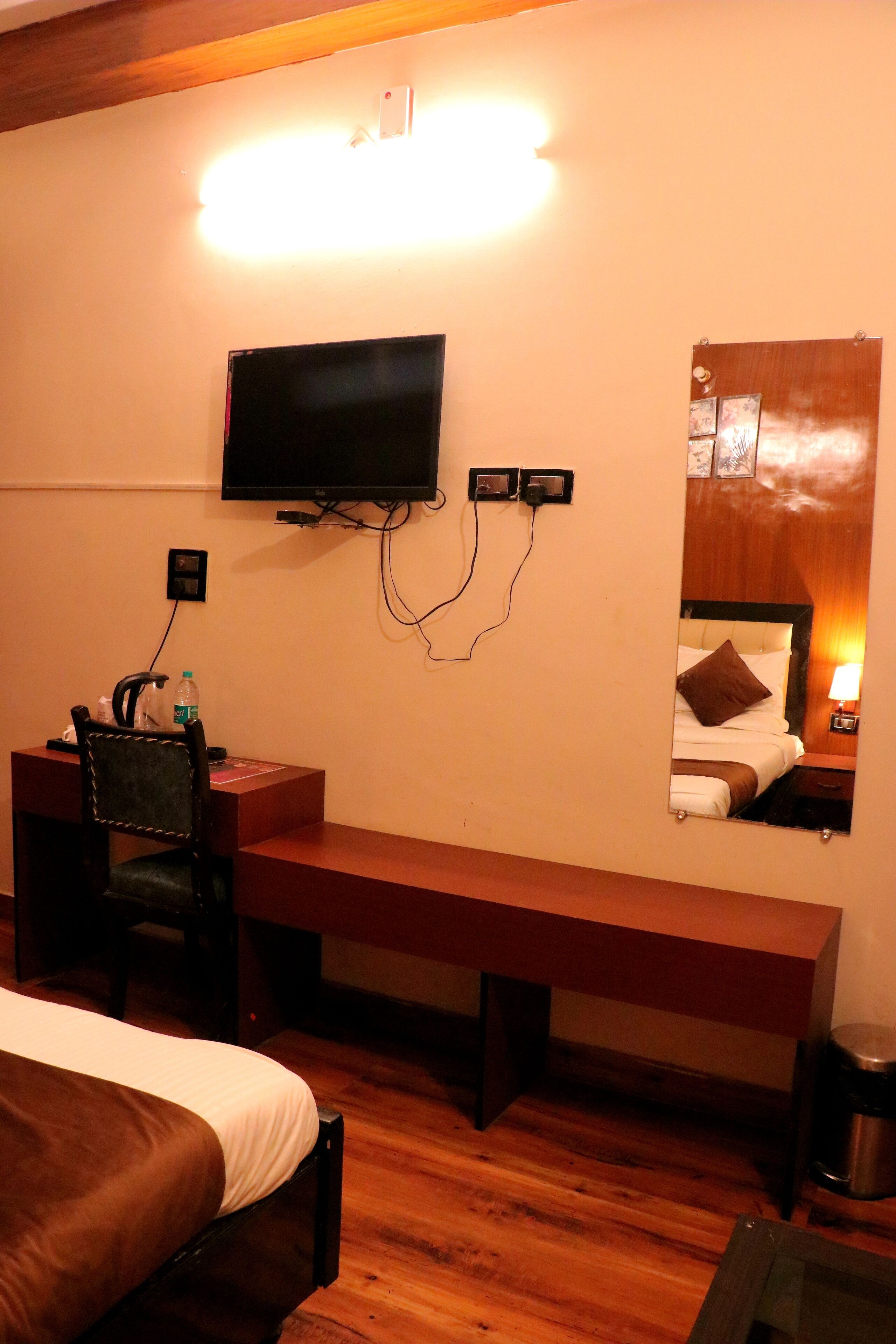 Camera d'albergo con un letto, una scrivania con sedia, una televisione a muro e uno specchio che riflette il letto e un comodino con lampada.