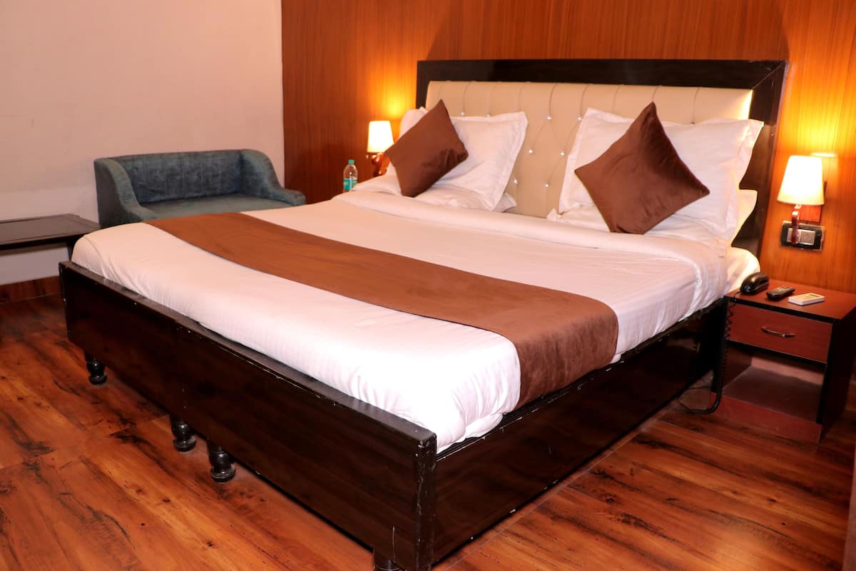 A neatly made bed with a wooden frame, a blue armchair, and a nightstand with a lamp.