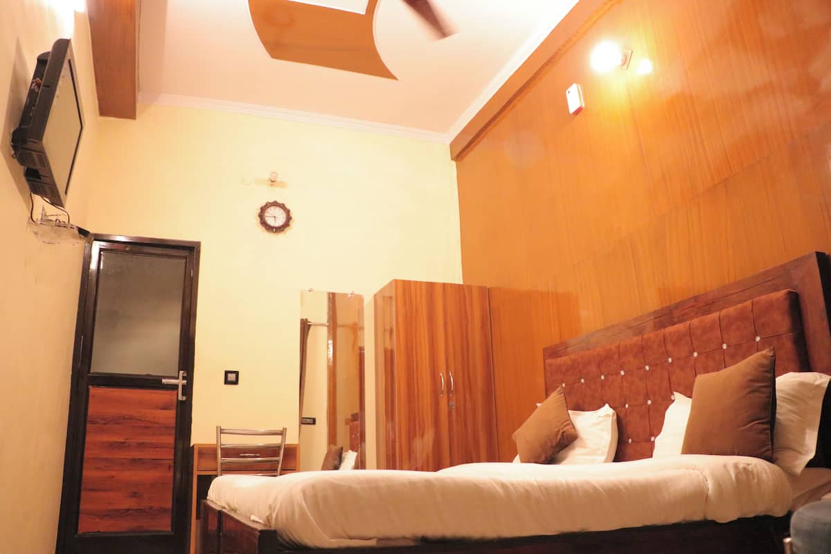 A bedroom with a wooden headboard, a bed with white bedding, a wooden wardrobe, and a small desk with a chair.