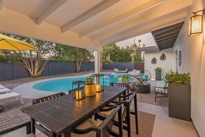Une terrasse extérieure avec une piscine, une table à manger et des chaises.