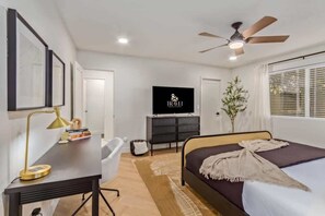 Une chambre à coucher comprenant un lit, un bureau, une chaise, une télévision, un ventilateur de plafond et une plante.