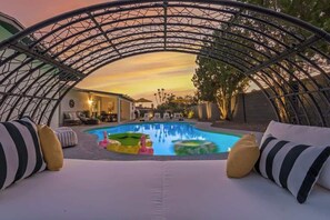 Ein Poolbereich mit Sonnensegel, Liegestühlen und Blick auf das Haus.