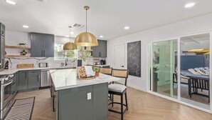 A modern kitchen with a central island, pendant lighting, and a view through a glass door to a dining area. - Casa Paradiso|Private Pool, Firepit & Putt. Green (Scottsdale)