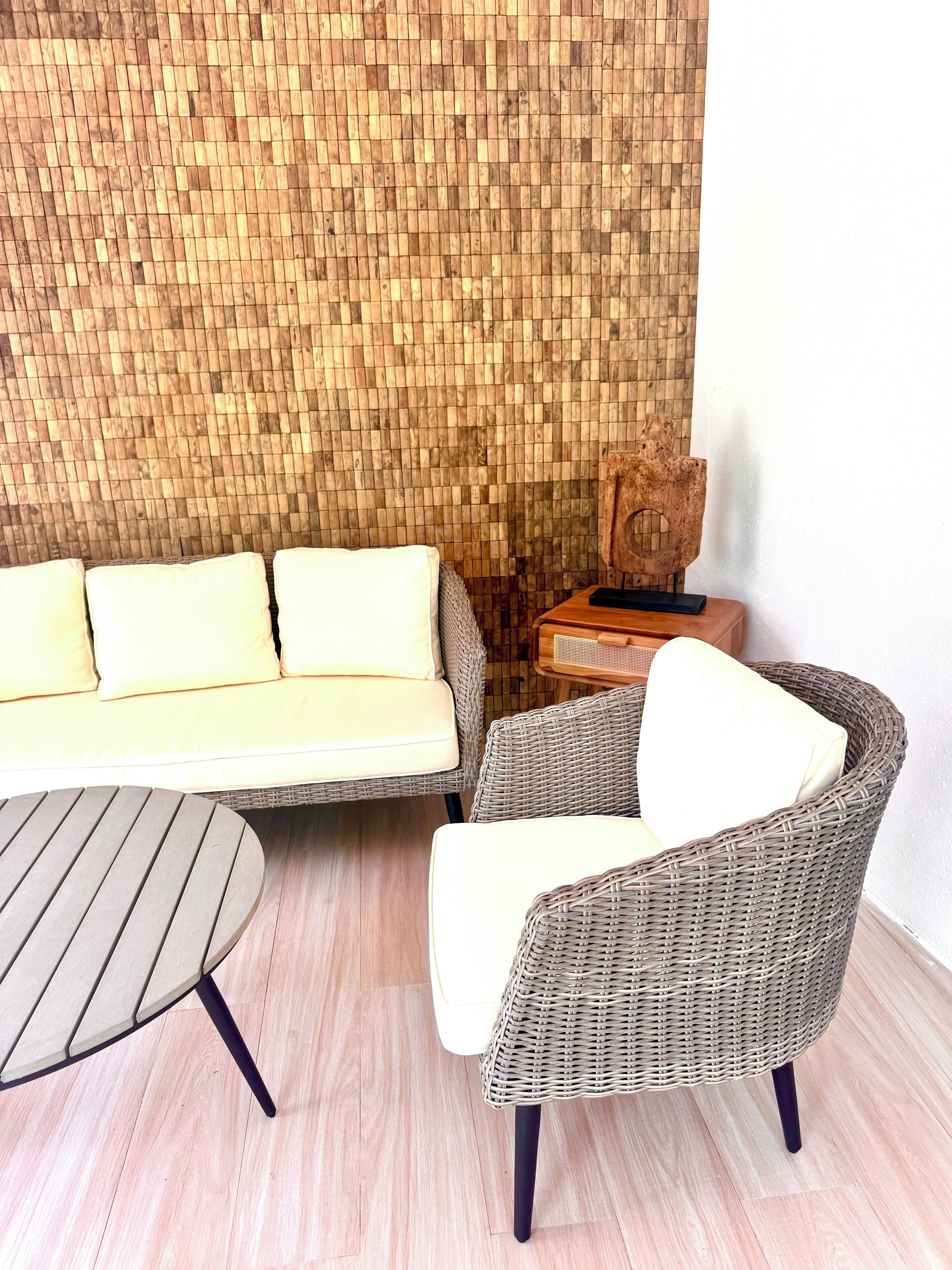 A room with a wicker sofa, a wicker armchair, a round table, and a wooden wall panel.