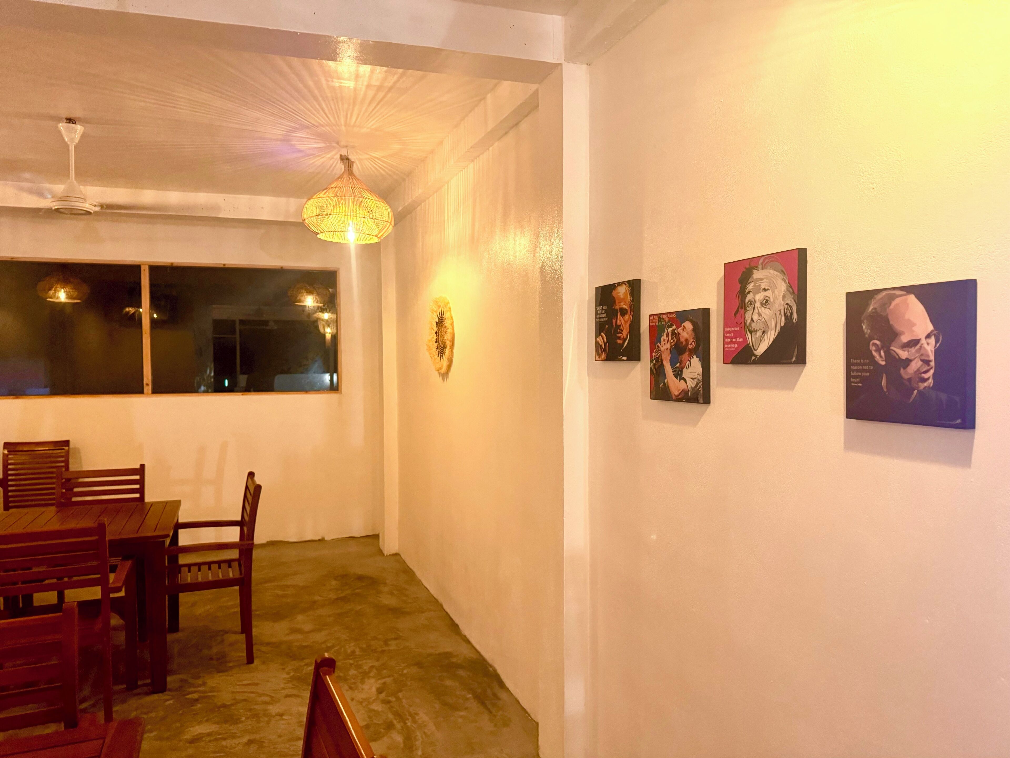 A room with a dining table and chairs, a ceiling fan, and wall-mounted artwork.