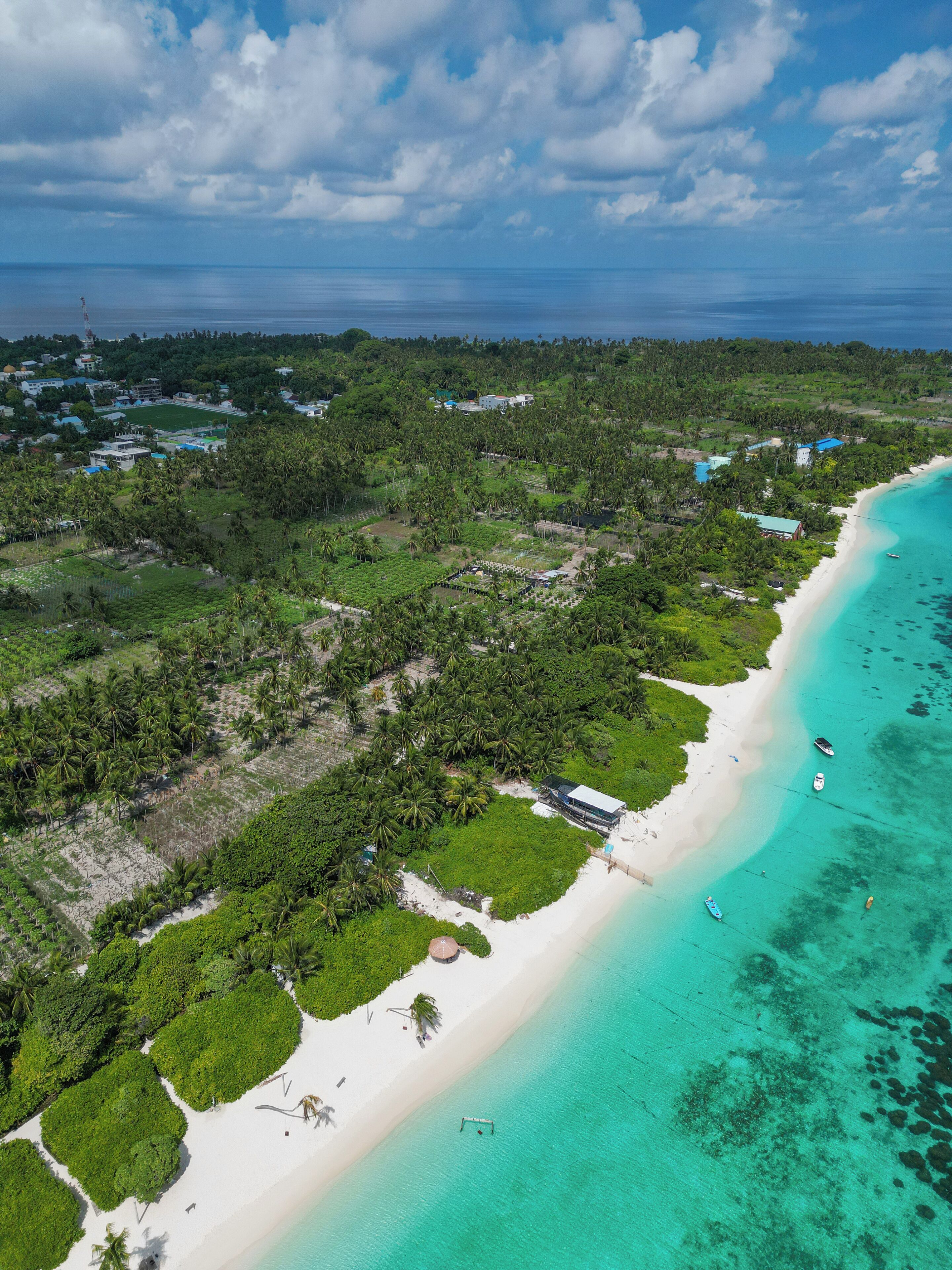 An aerial view of a tropical beach resort with a white sandy beach, clear turquoise waters, and lush greenery.