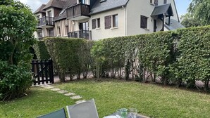 Un espace extérieur aménagé pour les repas, avec une table dressée pour quatre personnes, entouré d’une pelouse bien entretenue et d’une haie.
