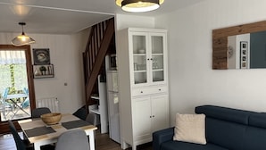 Un salon moderne avec un canapé bleu foncé, une table à manger en bois accompagnée de deux chaises, un meuble blanc et un escalier menant à un autre niveau.