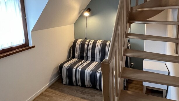 Une pièce avec un plafond en pente, un escalier en bois, un canapé à rayures et une fenêtre avec des rideaux.