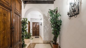 A hallway with a wooden door, potted plants, and a wall-mounted light fixture.