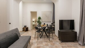 A modern living room with a grey sofa, a dining table with chairs, a TV on a stand, and a painting on the wall.