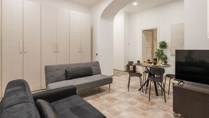 A modern living room with a grey sofa, a TV on a stand, and a dining area with chairs and a table.