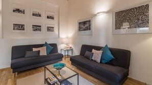 Una sala de estar moderna con dos sofás oscuros, una mesa de centro de vidrio y una mesita auxiliar.