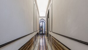 Un pasillo con piso a cuadros, paredes blancas y una puerta de cristal al final.