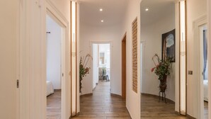 Un pasillo con suelo de madera, paredes blancas y una puerta que da a una habitación con cama.