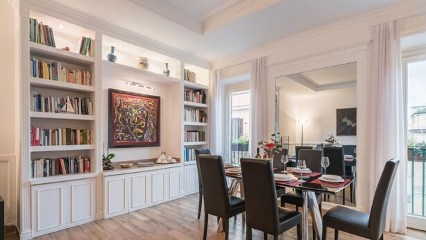 Un comedor amplio con una mesa larga y numerosas sillas, rodeado de estanterías llenas de libros y objetos decorativos.