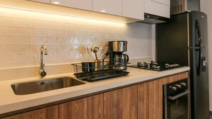 A modern kitchen with a stainless steel sink, a coffee maker, a gas stove, and a built-in oven. - w* | Executive 1BR Duplex in Miraflores (Miraflores)