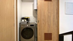 A laundry room with a washing machine and a dryer, wooden walls, and a vent on the wall. - w* | Executive 1BR Duplex in Miraflores (Miraflores)
