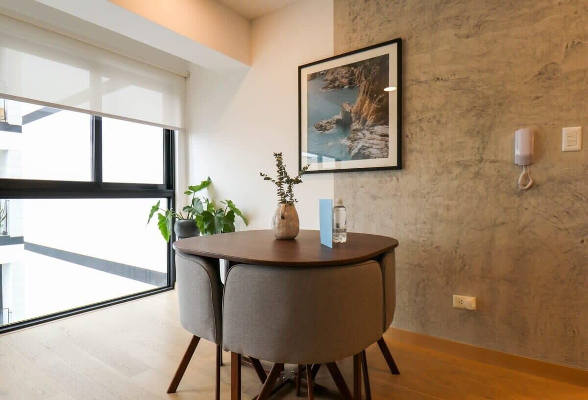 Une pièce moderne avec une table ronde, deux chaises, une plante en pot, un vase et un tableau encadré accroché au mur.
