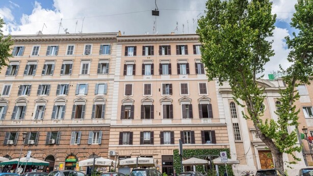 En byggnad med flera våningar i en klassisk arkitektonisk stil, med en rad butiker på bottenvåningen, inklusive en pizzeria och en restaurang.