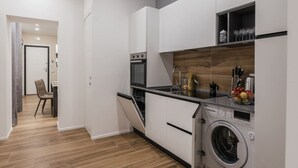 Une cuisine moderne avec des meubles blancs, un four encastré, un lave-vaisselle et une machine à laver.