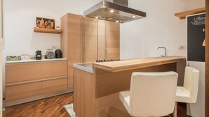 Een moderne keuken met houten kastjes, een roestvrijstalen afzuigkap, een houten aanrecht en een witte stoel.