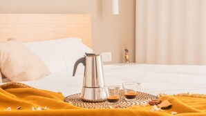 A neatly made bed with a white pillow, a metal coffee pot, and two glasses of coffee on a woven tray. - The Best Rent - Apartment in Buenos Aires district (Milano)