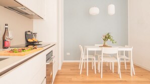 A modern kitchen with white cabinetry, a wooden countertop, a grill, and a dining area with a white table and chairs. - The Best Rent - Apartment in Buenos Aires district (Milano)