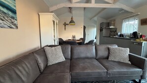 Ein modernes Wohnzimmer mit einem dunkelbraunen Ecksofa, einem Essbereich mit rundem Tisch und einer Küche im Hintergrund.