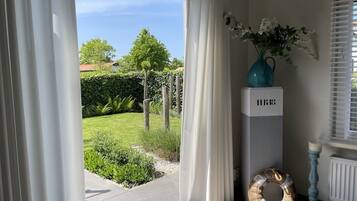 Une pièce dotée d’une porte-fenêtre coulissante donnant sur un jardin, d’un vase bleu rempli de fleurs, d’une armoire blanche et d’un panier en osier.