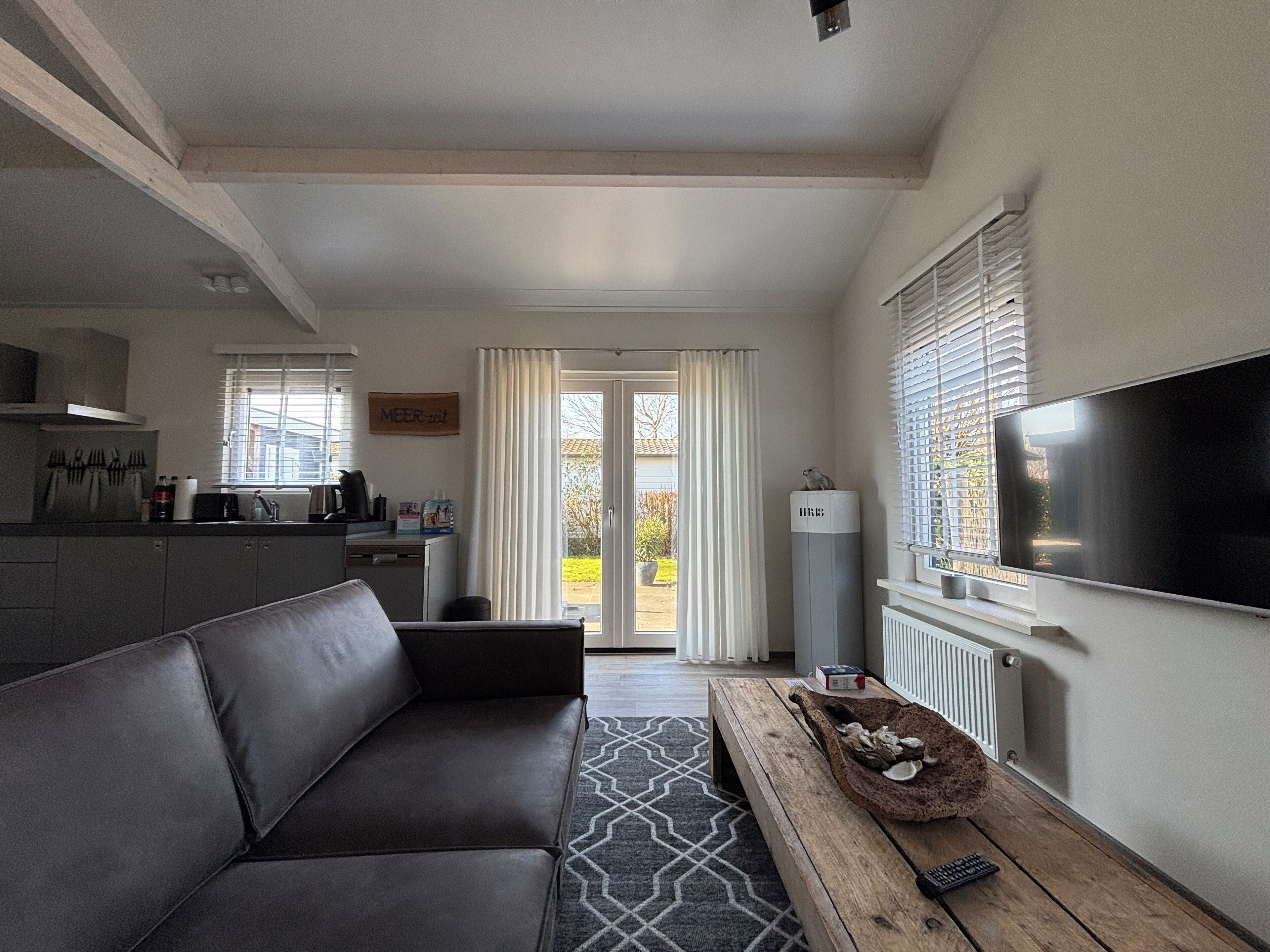 A modern living room with a sofa, a coffee table, a TV, and a kitchen area with a window.