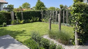 Ein gepflegter Garten mit befestigtem Weg, verschiedenen Sträuchern und einem Holzzaun.