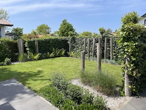 Um jardim bem cuidado com um caminho pavimentado, diversos arbustos e uma cerca de madeira.