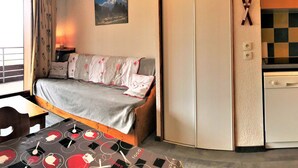 Ein gemütliches Zimmer mit Bett, Esstisch, Küchenzeile und Bergblick.
