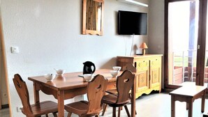 Ein Essbereich mit Holztisch und Stühlen, einem an der Wand montierten Fernseher und einem Fenster mit Blick ins Freie.