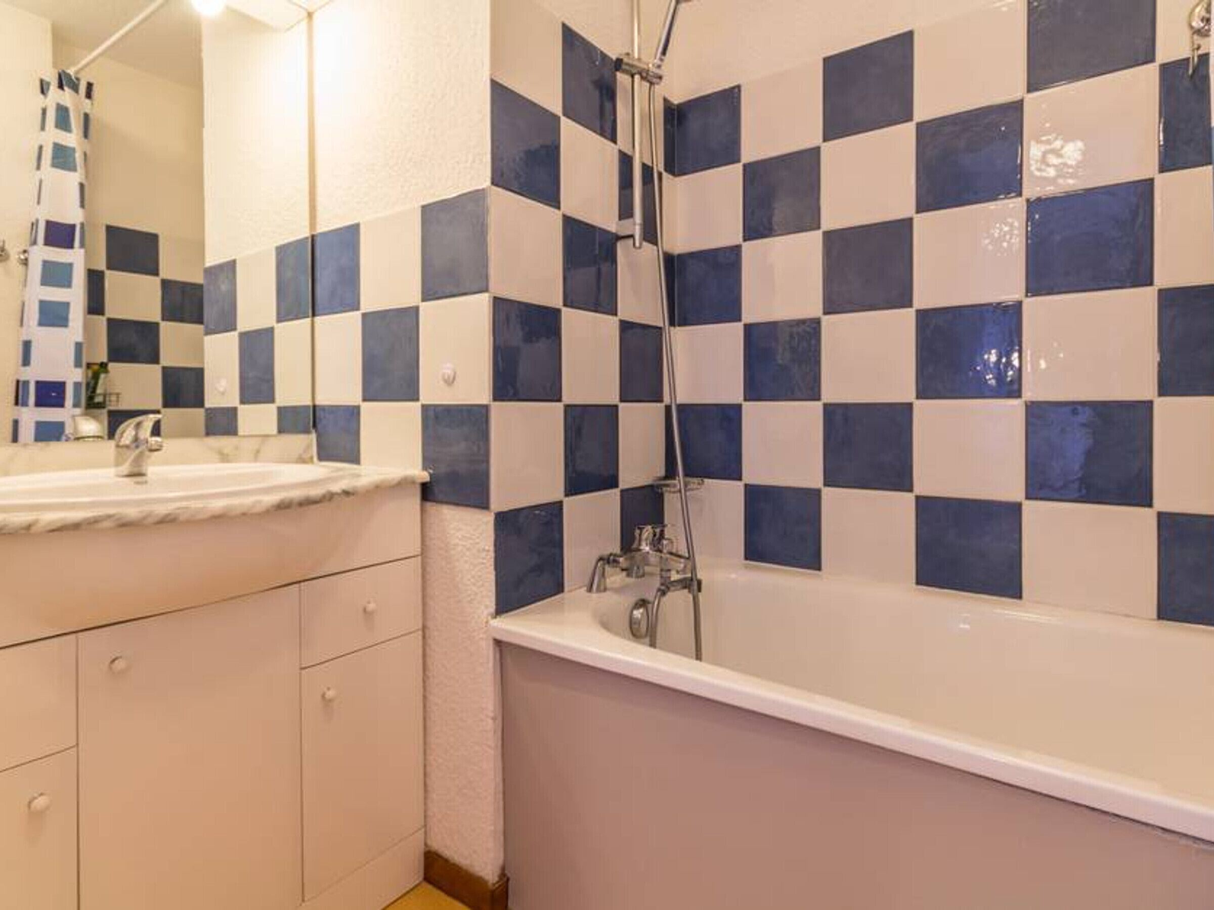 A bathroom with a checkered tile wall, a white sink, and a bathtub.