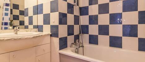 A bathroom with a checkered tile wall, a white sink, and a bathtub.