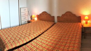 Ein Doppelbett mit einem gemusterten Bettbezug, ein Nachttisch mit Lampe und ein Kleiderschrank mit Schubladen.